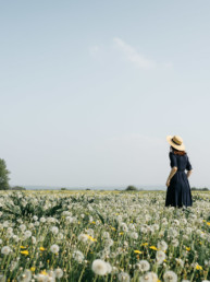 Girl with a hat standing in a field of dandelions