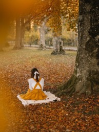 Girl sitting under an autumn tree reading a book