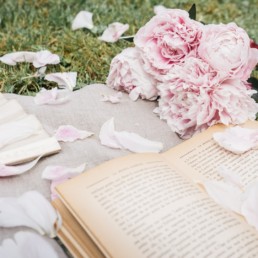 Peony petals scattered over a book and an antique fan