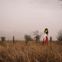 Girl standing in the middle of an empty and foggy field