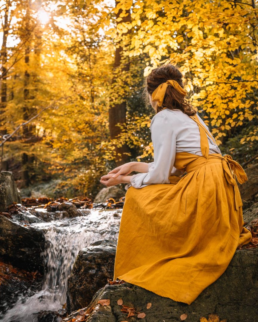 Girl wearing a linen pinafore dress by Isona Linen in the forest during autumn