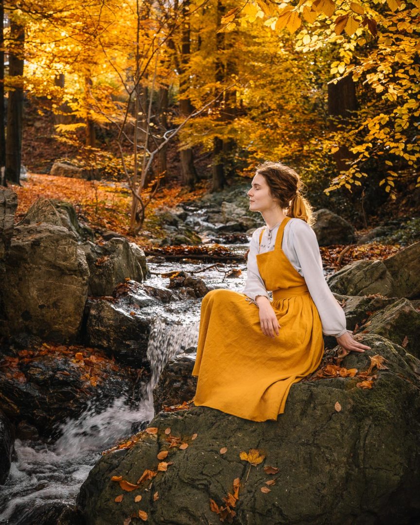 Girl wearing a linen pinafore dress by Isona Linen in the forest during autumn