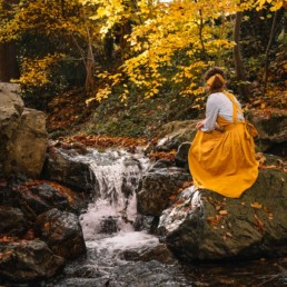 Girl in a dress sitting on top of a rock next to a river