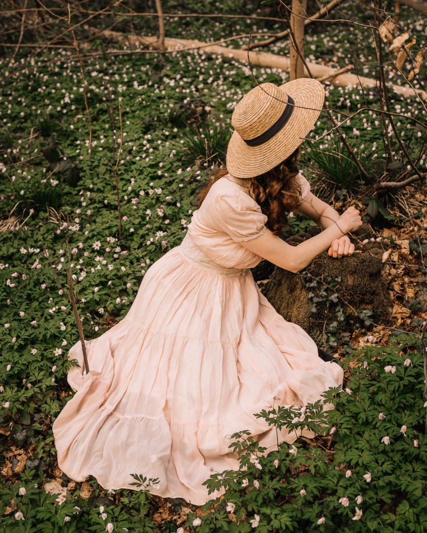 A girl in a 1930s dress sitting among the wood anemone.