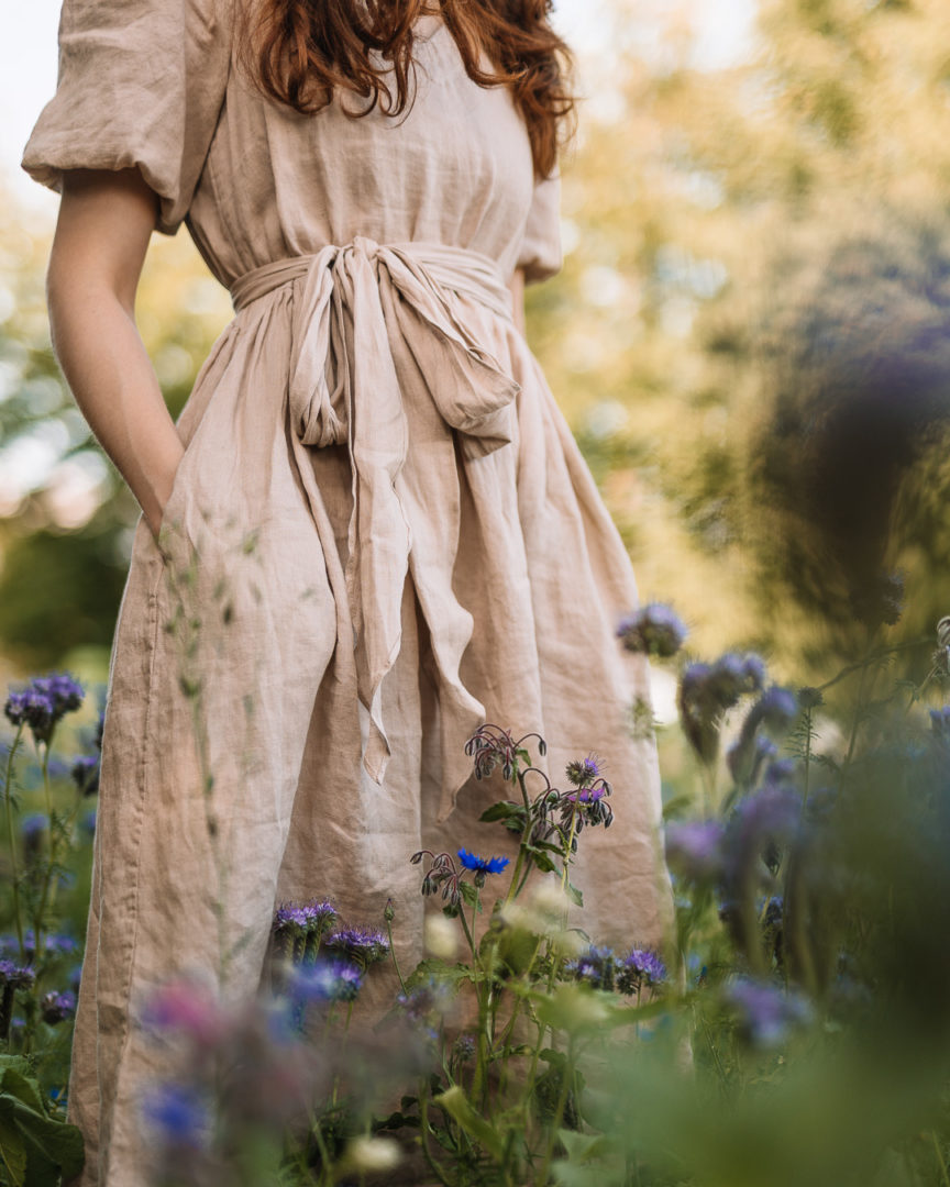 Close up shot of a girl wearing a TwoLINEN puff-sleeved linen dress in a field of blue wildflowers