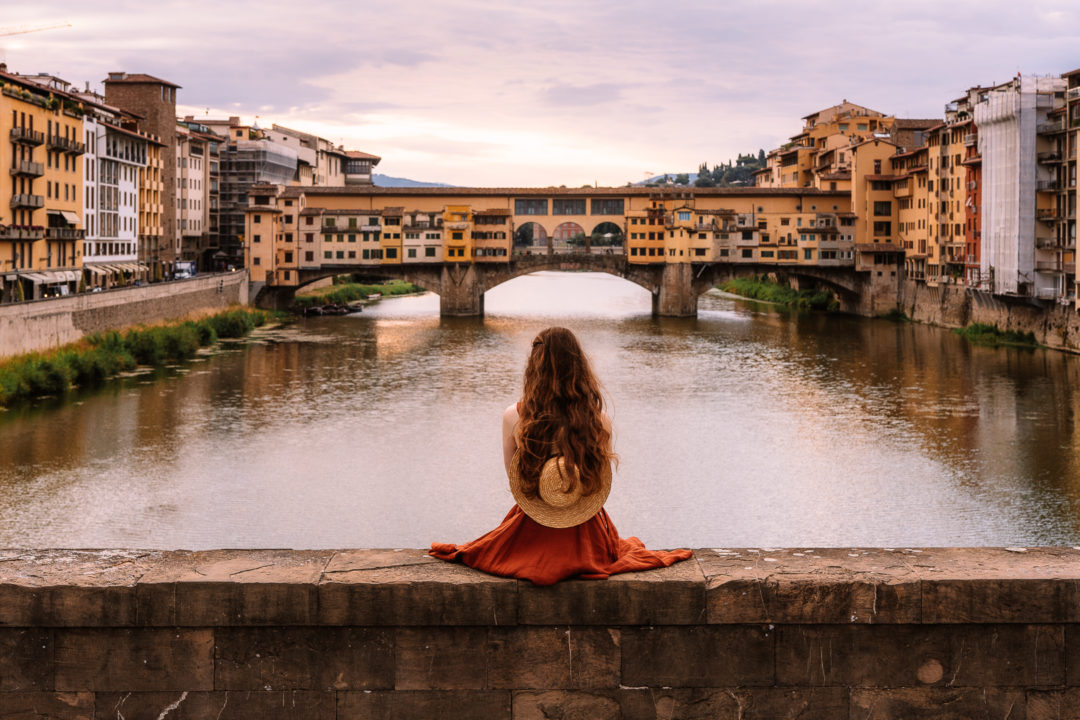 woman sitting on a bridge overlooking ponte vecchio in florence