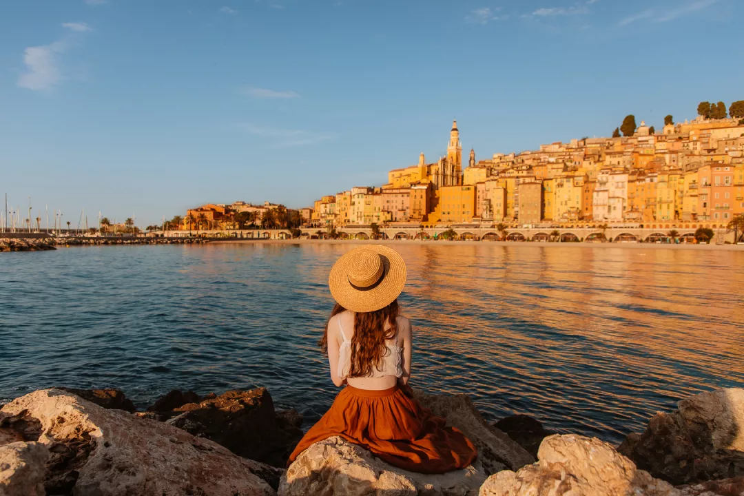 woman sitting on a cliff looking at menton at sunrise